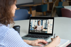 Teen girl student watching webinar, distance learning on video call with african online teacher or virtual tutor studying university seminar having online meeting on laptop screen. Over shoulder view