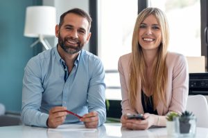 Portrait of cute couple explaing something looking at camera while doing video call in the office at home.